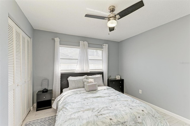 bedroom featuring baseboards, light wood-style flooring, ceiling fan, a closet, and a textured ceiling