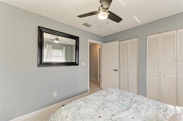 bedroom featuring visible vents, two closets, baseboards, wood finished floors, and a textured ceiling