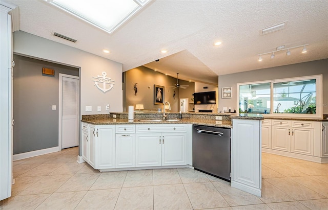 kitchen featuring visible vents, a sink, dark stone counters, dishwashing machine, and vaulted ceiling