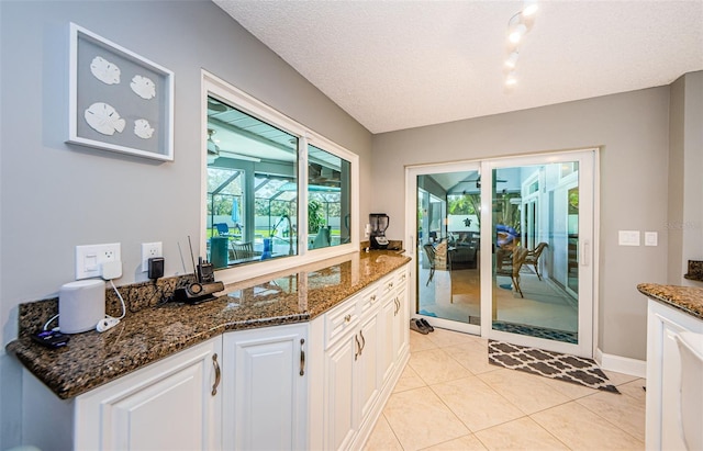 kitchen featuring dark stone countertops, a textured ceiling, white cabinets, light tile patterned floors, and baseboards