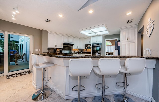 kitchen with under cabinet range hood, visible vents, a kitchen breakfast bar, and white cabinetry