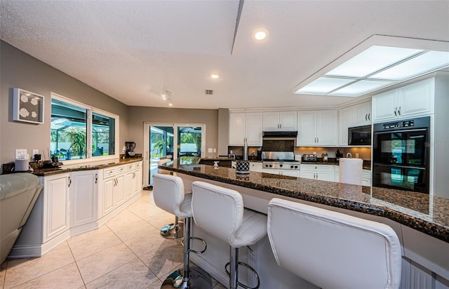 kitchen with under cabinet range hood, light tile patterned floors, recessed lighting, white cabinets, and black appliances