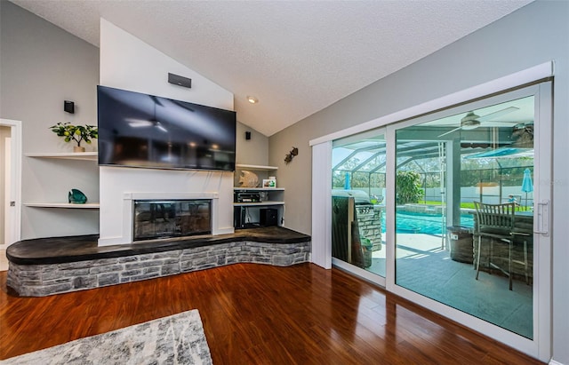 unfurnished living room featuring ceiling fan, vaulted ceiling, a fireplace, wood finished floors, and a textured ceiling