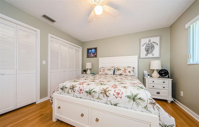 bedroom with visible vents, multiple closets, light wood-style floors, and a textured ceiling