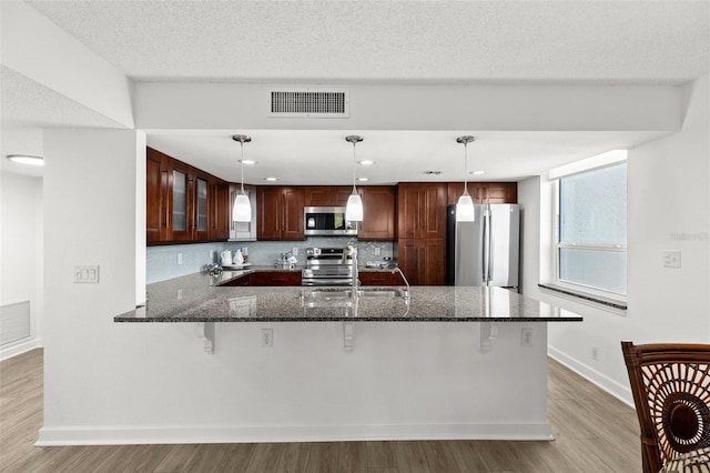 kitchen featuring visible vents, glass insert cabinets, dark stone counters, light wood-type flooring, and stainless steel appliances