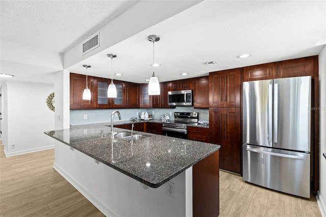 kitchen featuring visible vents, light wood finished floors, a peninsula, a sink, and stainless steel appliances