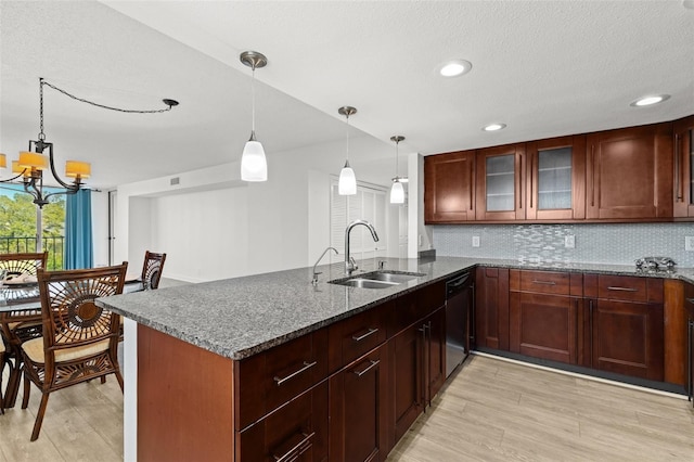 kitchen featuring dishwashing machine, a peninsula, a sink, a notable chandelier, and tasteful backsplash