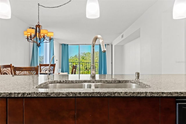 kitchen with a sink, decorative light fixtures, an inviting chandelier, light stone countertops, and dark brown cabinets