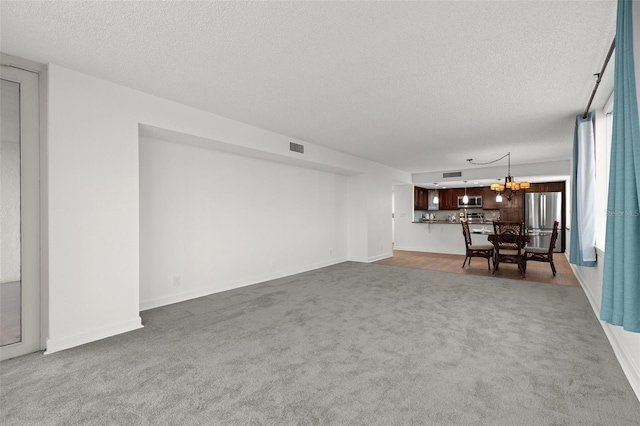 unfurnished living room featuring baseboards, visible vents, carpet floors, an inviting chandelier, and a textured ceiling