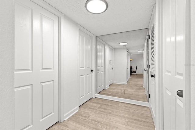 corridor with baseboards, light wood-type flooring, and a textured ceiling