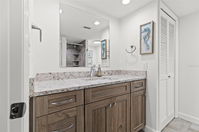 bathroom with visible vents, a closet, tiled shower, baseboards, and vanity