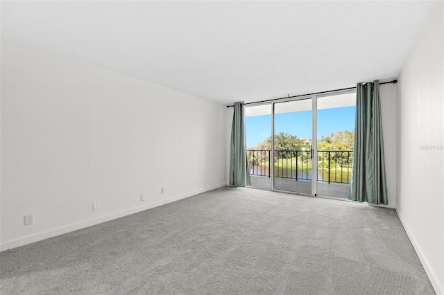 carpeted empty room featuring a wall of windows and baseboards