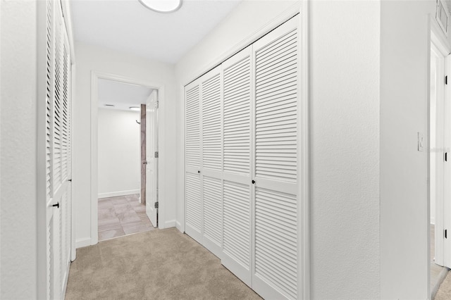 corridor featuring baseboards and light colored carpet