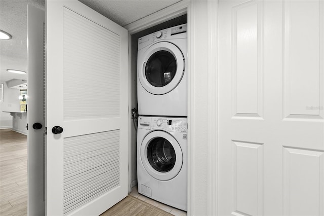 clothes washing area featuring baseboards, laundry area, light wood-style flooring, stacked washer and clothes dryer, and a textured ceiling