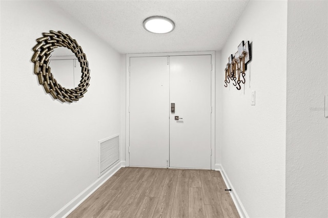 entryway with light wood-type flooring, visible vents, baseboards, and a textured ceiling