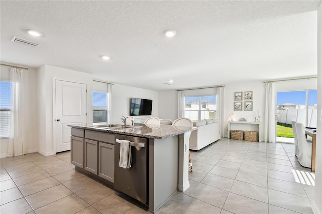 kitchen featuring stainless steel dishwasher, light tile patterned floors, visible vents, and a sink