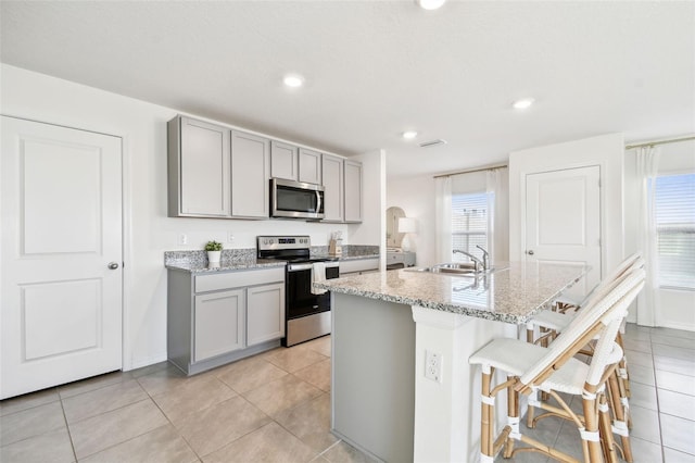 kitchen with a sink, stainless steel appliances, light stone counters, and gray cabinets