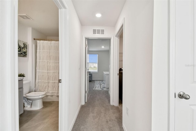 hallway featuring light tile patterned floors, visible vents, light carpet, and baseboards