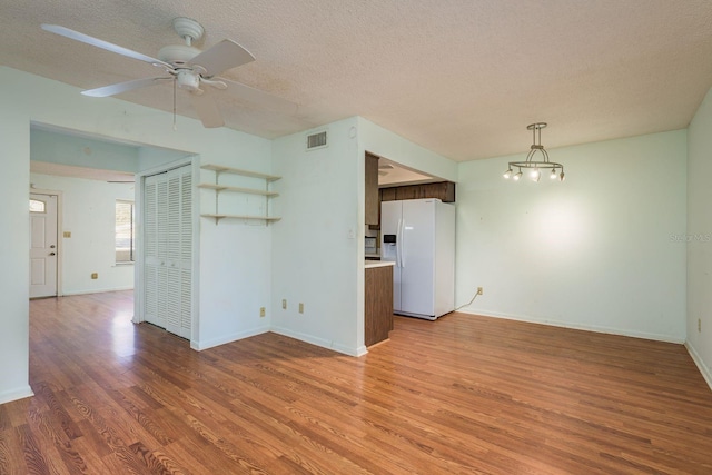 spare room featuring ceiling fan with notable chandelier, light wood-style floors, visible vents, and a textured ceiling