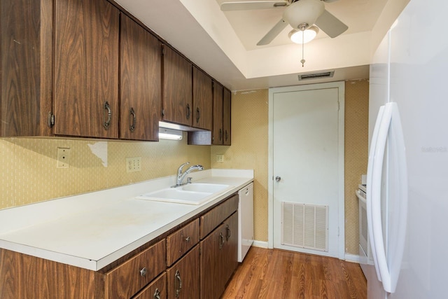 kitchen featuring visible vents, white appliances, light wood-style floors, and a sink