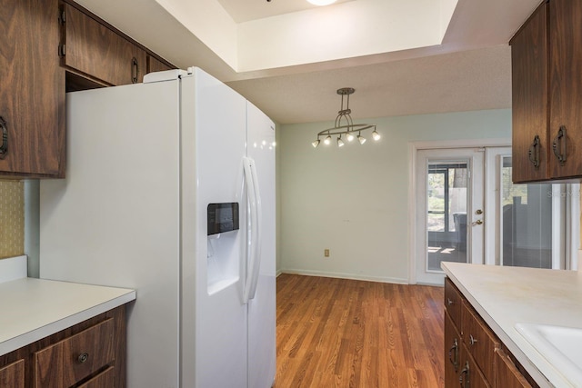 kitchen with baseboards, light wood finished floors, light countertops, white fridge with ice dispenser, and pendant lighting