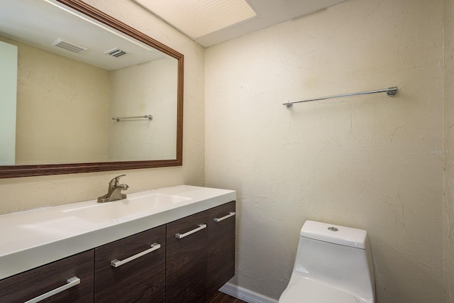 bathroom featuring visible vents, toilet, vanity, and a textured wall