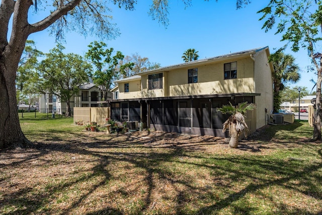 rear view of house with a yard, fence, a sunroom, and stucco siding