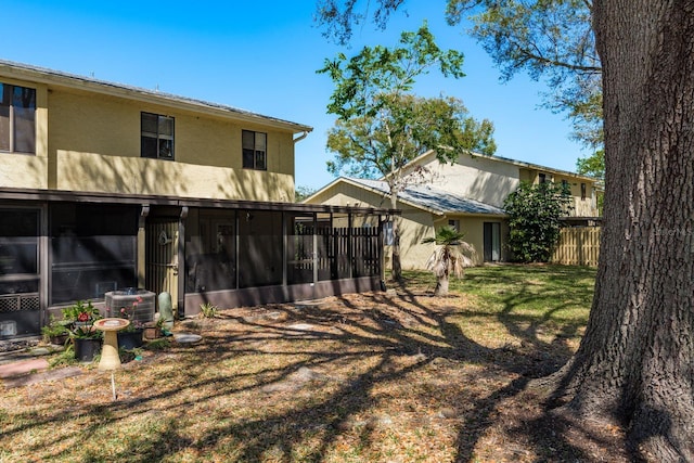 rear view of property featuring fence, stucco siding, a lawn, cooling unit, and a sunroom