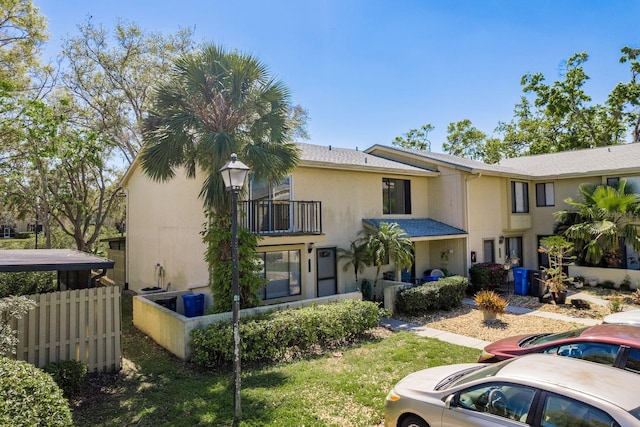 view of front of property featuring stucco siding, a balcony, and fence