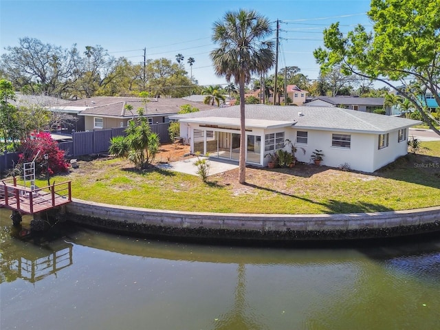 back of property with stucco siding, a water view, a lawn, and fence