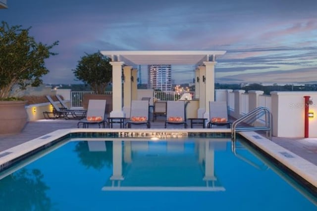 pool at dusk featuring a community pool, a patio area, and a pergola