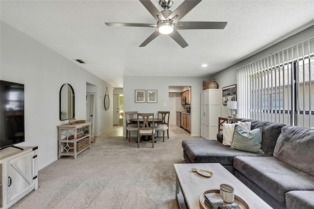 living area featuring visible vents, light carpet, a textured ceiling, baseboards, and ceiling fan