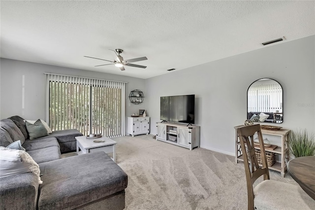 living room featuring a ceiling fan, light colored carpet, visible vents, and a textured ceiling