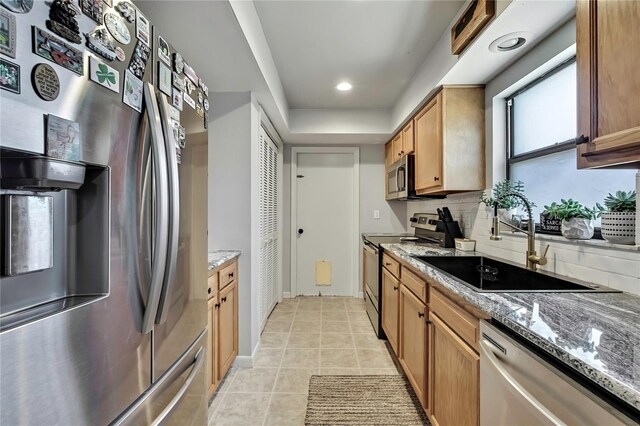 kitchen featuring a sink, tasteful backsplash, appliances with stainless steel finishes, light tile patterned floors, and light stone countertops