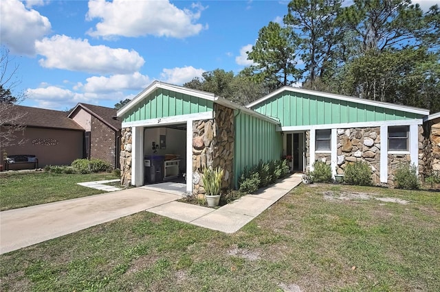 view of front of house featuring a front yard, driveway, stone siding, a garage, and board and batten siding