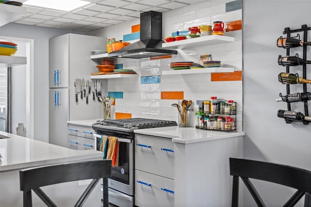 kitchen with gas range, decorative backsplash, range hood, a paneled ceiling, and open shelves