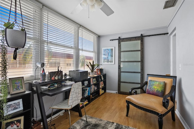 office space featuring visible vents, baseboards, ceiling fan, a barn door, and wood finished floors