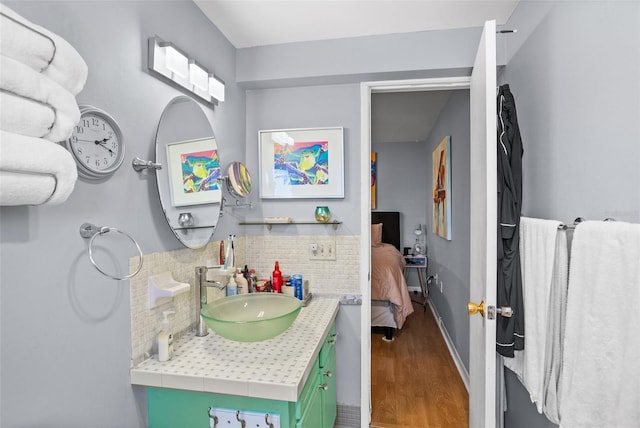 bathroom with ensuite bath, wood finished floors, decorative backsplash, baseboards, and vanity