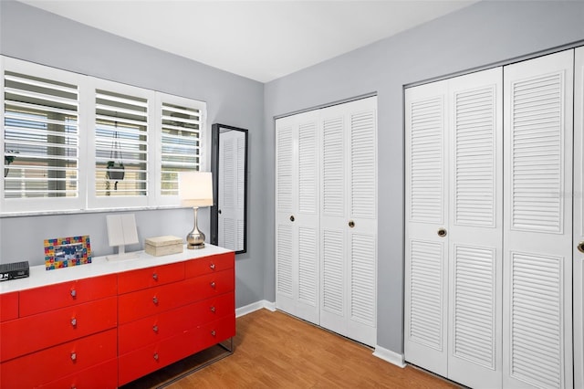 bedroom with light wood finished floors, two closets, and baseboards