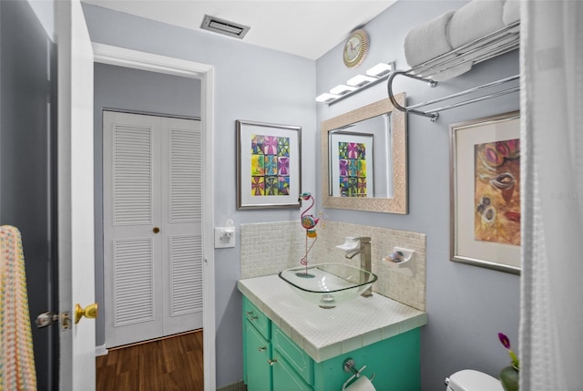 bathroom featuring vanity, wood finished floors, visible vents, decorative backsplash, and toilet