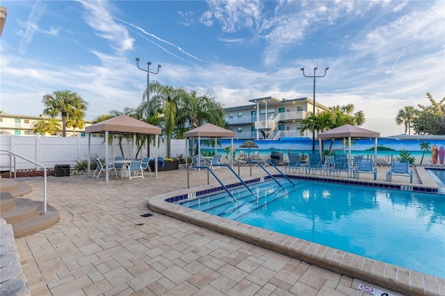 community pool with a gazebo, fence, and a patio area