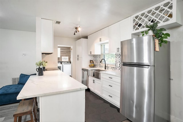 kitchen with a sink, backsplash, washing machine and dryer, stainless steel appliances, and a breakfast bar area