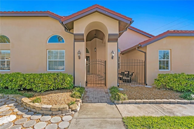 entrance to property with a gate, fence, and stucco siding