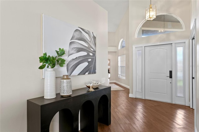 foyer entrance with an inviting chandelier, a high ceiling, wood finished floors, and baseboards