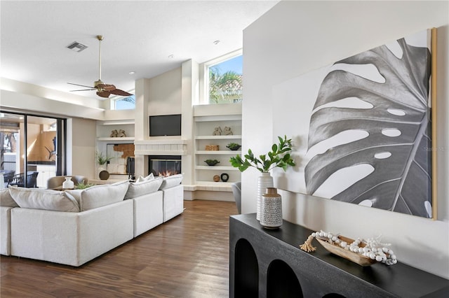 living room with visible vents, built in shelves, a glass covered fireplace, wood finished floors, and ceiling fan