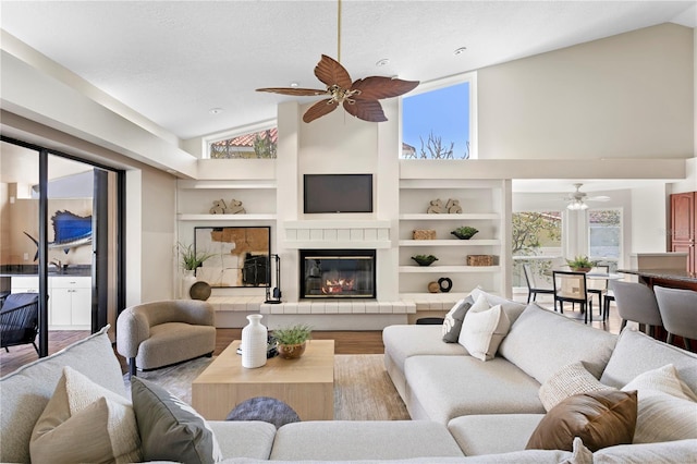 living room featuring built in shelves, a textured ceiling, a ceiling fan, and wood finished floors