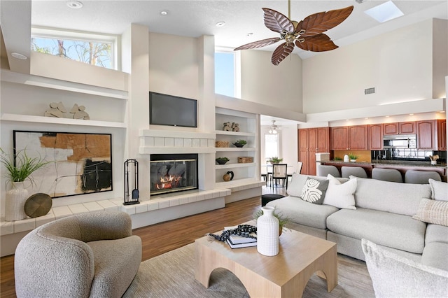 living room featuring built in shelves, a ceiling fan, visible vents, light wood-style floors, and a tiled fireplace