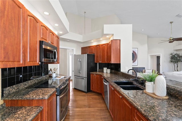 kitchen featuring a sink, wood finished floors, dark stone counters, appliances with stainless steel finishes, and ceiling fan