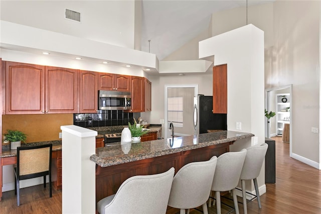 kitchen featuring visible vents, a peninsula, stainless steel appliances, dark wood-type flooring, and a kitchen bar