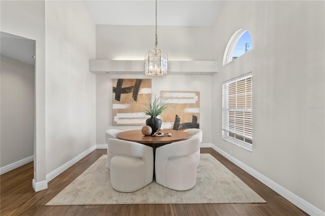 dining area with baseboards, a notable chandelier, a high ceiling, and wood finished floors